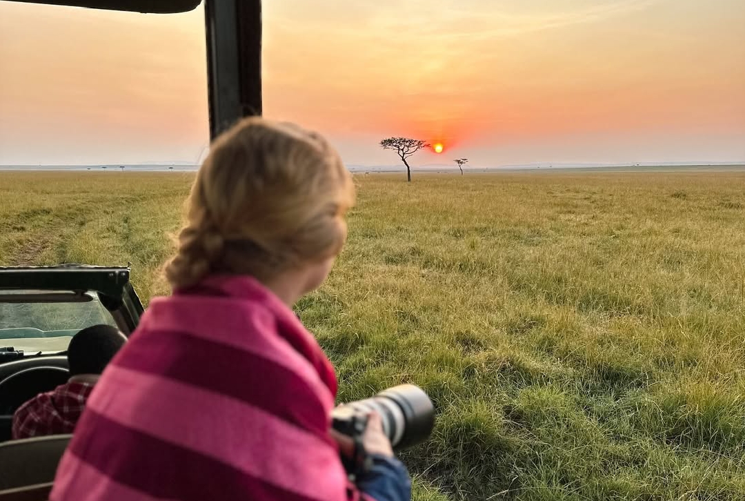 Traveler in an open safari vehicle watching the sunrise over the maasai mara savannah